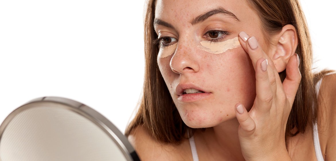 Junge Frau trägt hellen Concealer unter ihren Augen auf.
